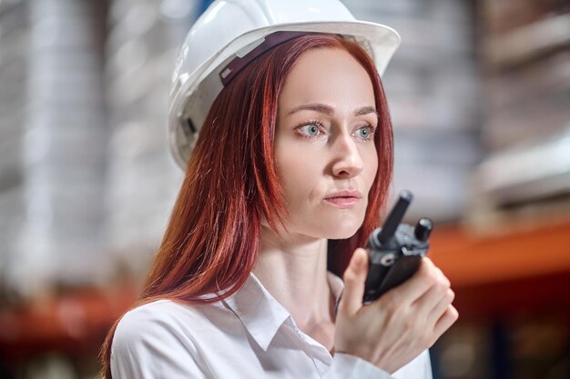 Woman in protective helmet listening to walkie-talkie in hand