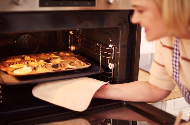 Free photo woman pulls muffins from the oven