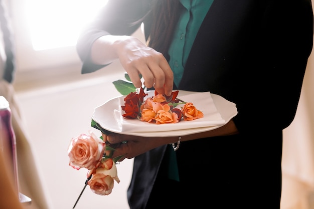 Free Photo woman puts delicate orange rose buds on the white plate