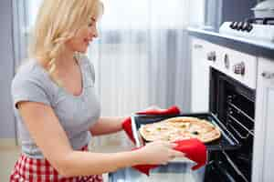 Free photo woman putting pizza into oven