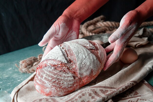 Woman putting whole homemade bread with hands on the brown towel. flour on the bread. 