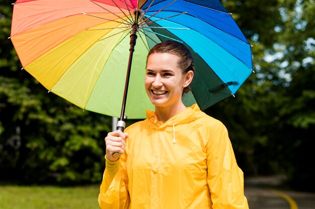 Woman in rain coat smiling while holding an umbrella