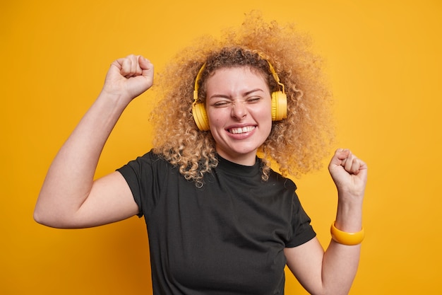 Free Photo woman raises arms feels upbeat dances with rhythm of music chills indoor wears stereo headphones casual black t shirt 