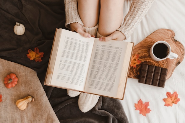 Woman reading book near snack and autumn symbols