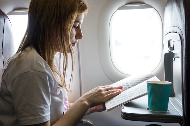 Free Photo woman reading a book in a plane