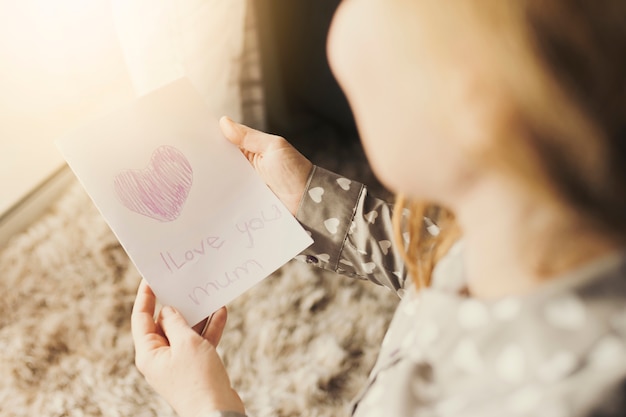 Free Photo woman reading greeting card with i love you mum inscription 