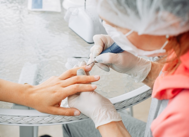 A woman receiving manicure from a woman in gloves and mask in beauty salon during daytime