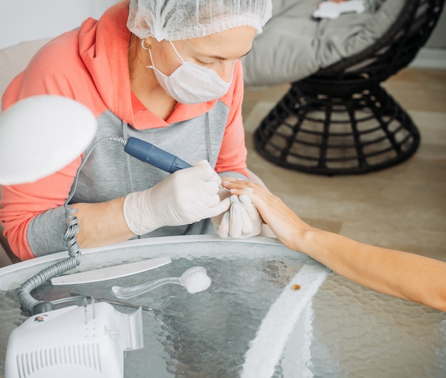 A woman receiving manicure from a woman in gloves and mask in beauty salon during daytime