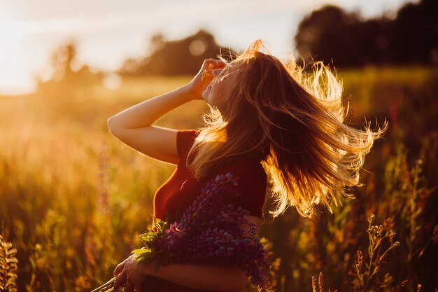 Woman in red dress whirls in the rays of evening sun 