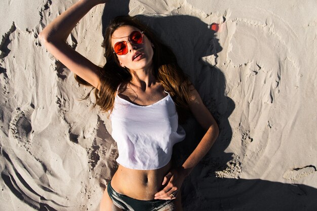 Woman in red sunglasses lies on a white beach