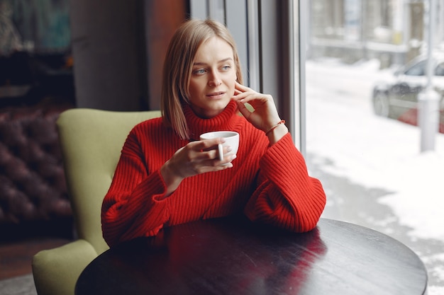 Woman in a red sweater. Lady drinks a coffee.