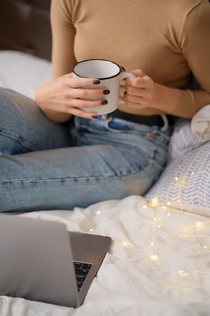 Free photo woman relaxing and drinking cup of hot coffee or tea using laptop computer in the bedroom.