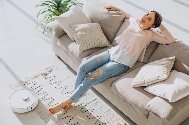 Free Photo woman relaxing on sofa while robot vacuum cleaner doing housework