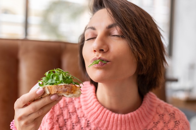 Woman in a restaurant in a cozy warm sweater wholesome breakfast with toast with arugula and salmon