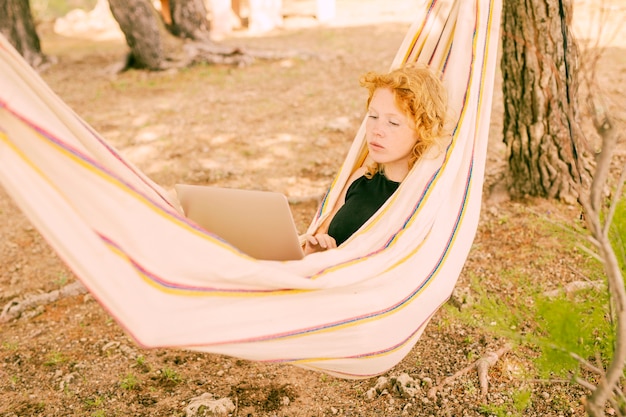 Free photo woman resting in hammock with laptop