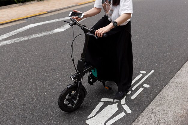 Woman riding electric bicycle in the city and holding smartphone