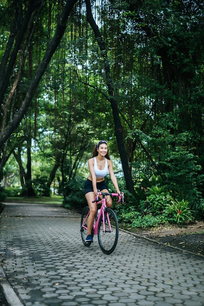 Woman riding a road bike in the park. Portrait of young beautiful woman on pink bike.