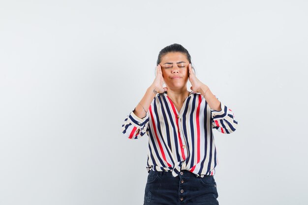 woman rubbing her temples in shirt, skirt and looking tired