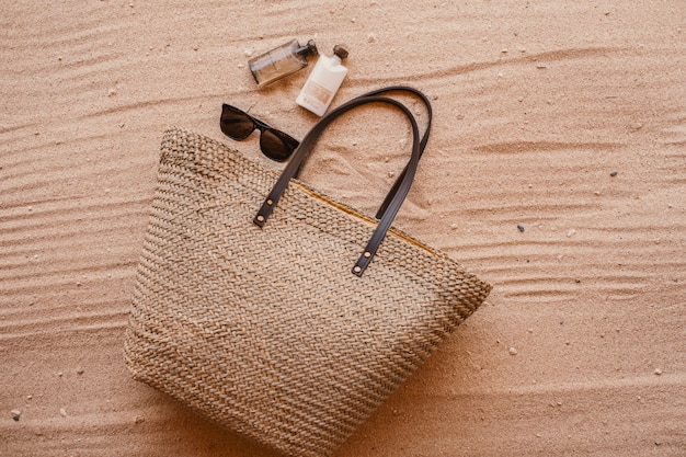 Woman's bag next to  perfume and sunglasses put on sand