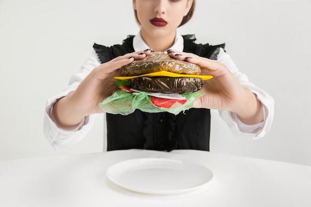 Woman's eating burger made of plastic, eco concept.