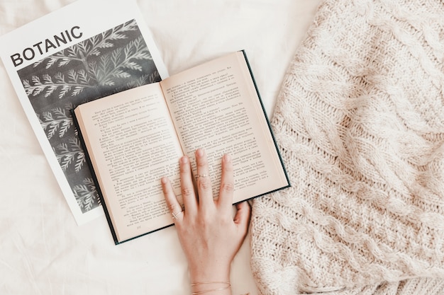 Free photo woman's hand being on book lying on banner and blanket on bedsheet