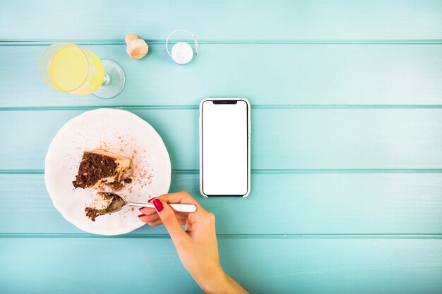 Woman's hand eating pastry with drink and cellphone on table