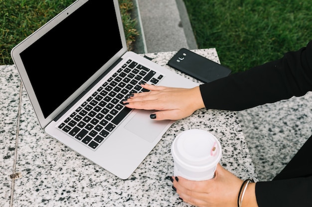 Woman's hand holding disposable coffee cup typing on laptop