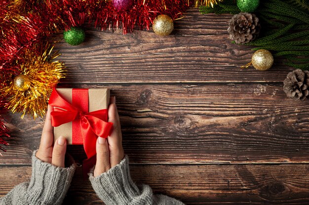 Woman's hand holding a gift box with red ribbon on wooden floor