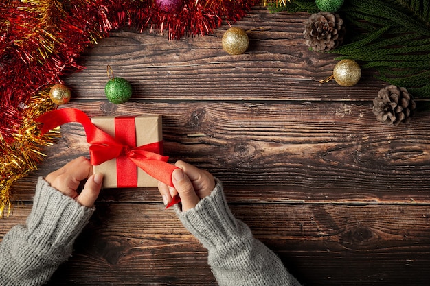 Woman's hand holding a gift box with red ribbon on wooden floor