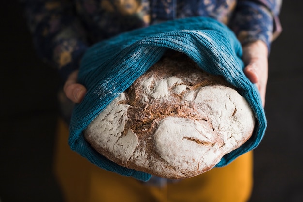 Woman's hand holding large freshly baked bread covered in blue napkin