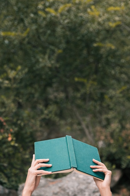 Free photo woman's hand holding an open book in hand against green trees