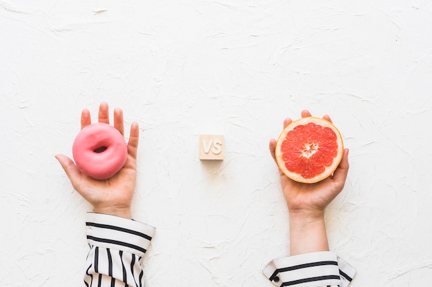 Free Photo woman's hand holding pink donut versus grapefruit slice over textured backdrop