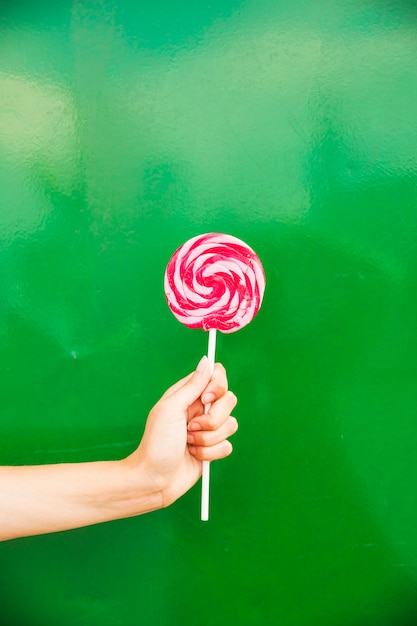 Free photo woman's hand holding red and pink lollipop in hand against green background