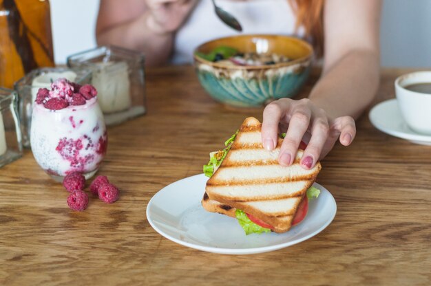 Woman's hand holding sandwich from white plate on wooden table