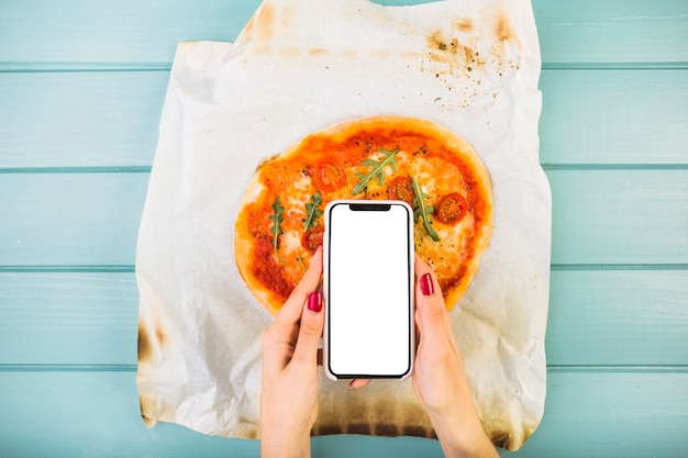 Free photo woman's hand holding smartphone over pizza