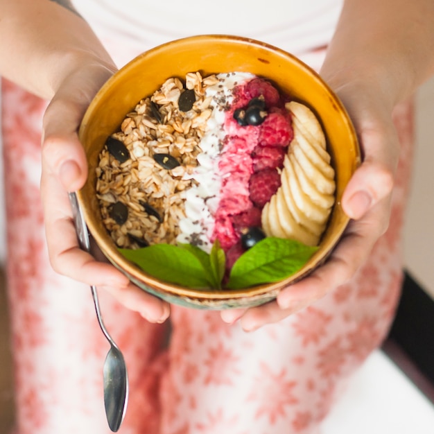 Free Photo woman's hand holding tasty oatmeal with berries and banana slices in bowl