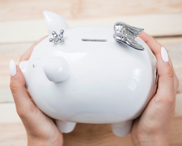 Free Photo woman's hand holding white ceramic piggybank with silver crown and wings