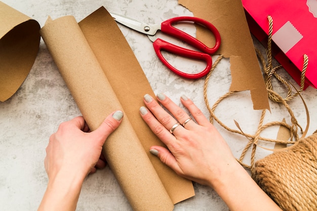 Free photo woman's hand making the craft with brown paper on textured backdrop