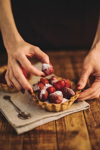 Free photo woman's hand making strawberries tart on wooden table