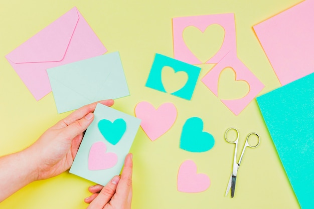 Free photo woman's hand preparing heart shape greeting card on yellow background