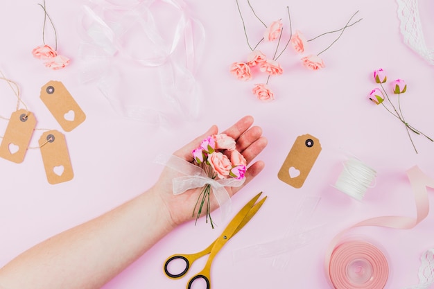 Woman's hand showing the artificial flowers with ribbon on pink background