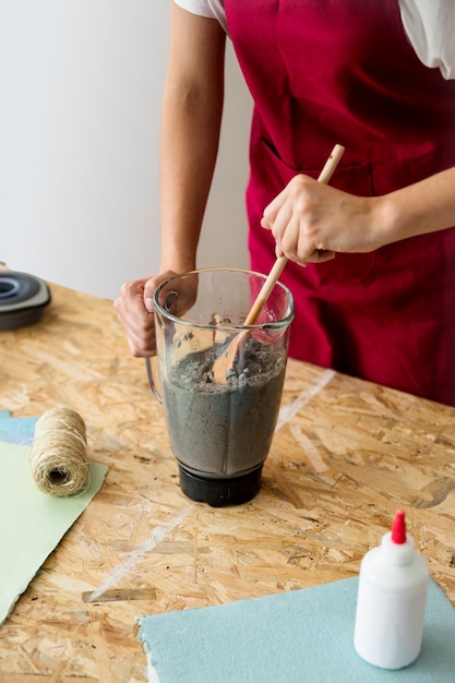 Woman's hand stirring paper pulp with ladle in blender