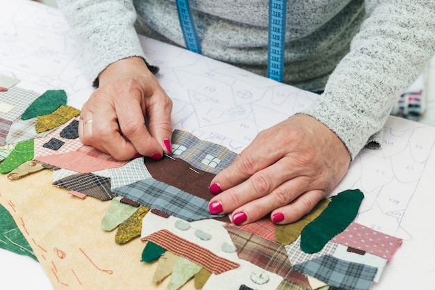 Free photo woman's hand stitching fabric house with needle at workplace