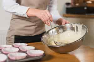 Free photo woman's hand taking cake mix with ladle from the stainless steel bowl