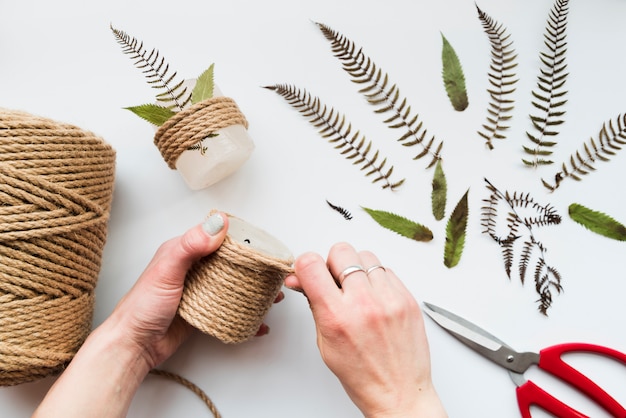 Free Photo woman's hand wrapping the string on candle with leaves and scissor on white background