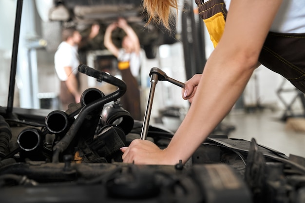 Woman's hands repairing car under hood with tool.