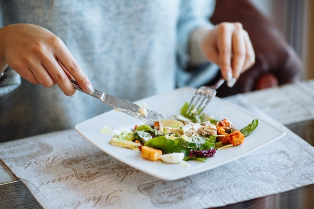 Woman's hands with Caesar salad on table in restaurant