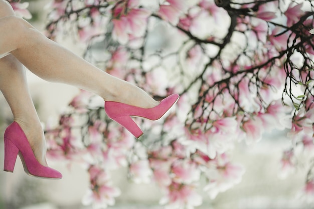 Free photo woman's legs in the pink shoes on the blossom magnolia tree