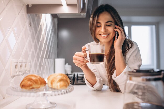 Woman's morning with phone,croissant and coffee at kitchen