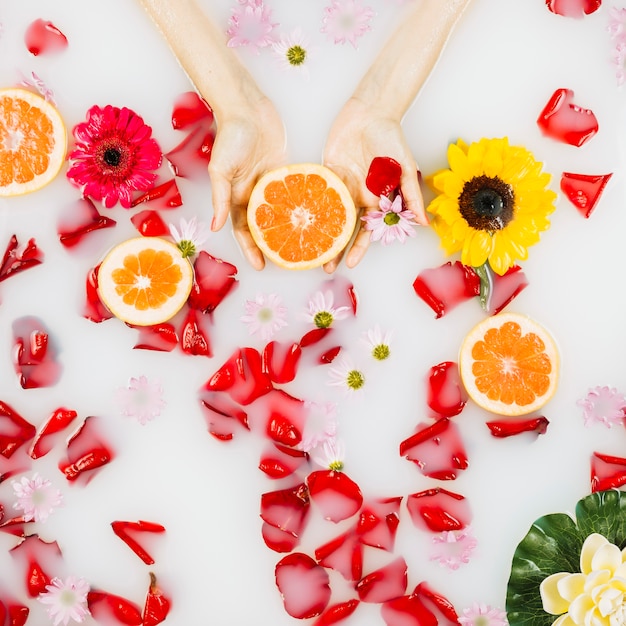 Woman's palm with grapefruit, petals and flowers on clear white water